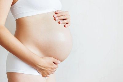 Eine schwangere Frau streichelt sanft mit beiden Händen ihren runden Bauch